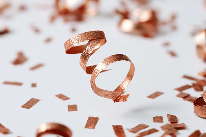 Copper metallic streamers and confetti pieces falling mid-air against a white background