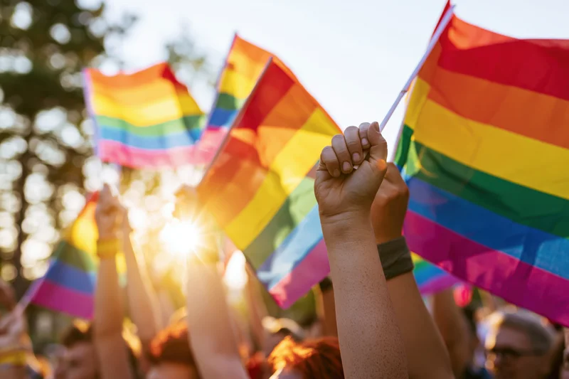 People raising rainbow pride flags in a sunny outdoor demonstration