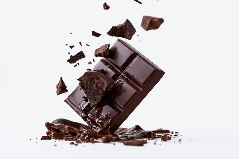 Dark chocolate bar breaking apart midair with chunks scattering against white background