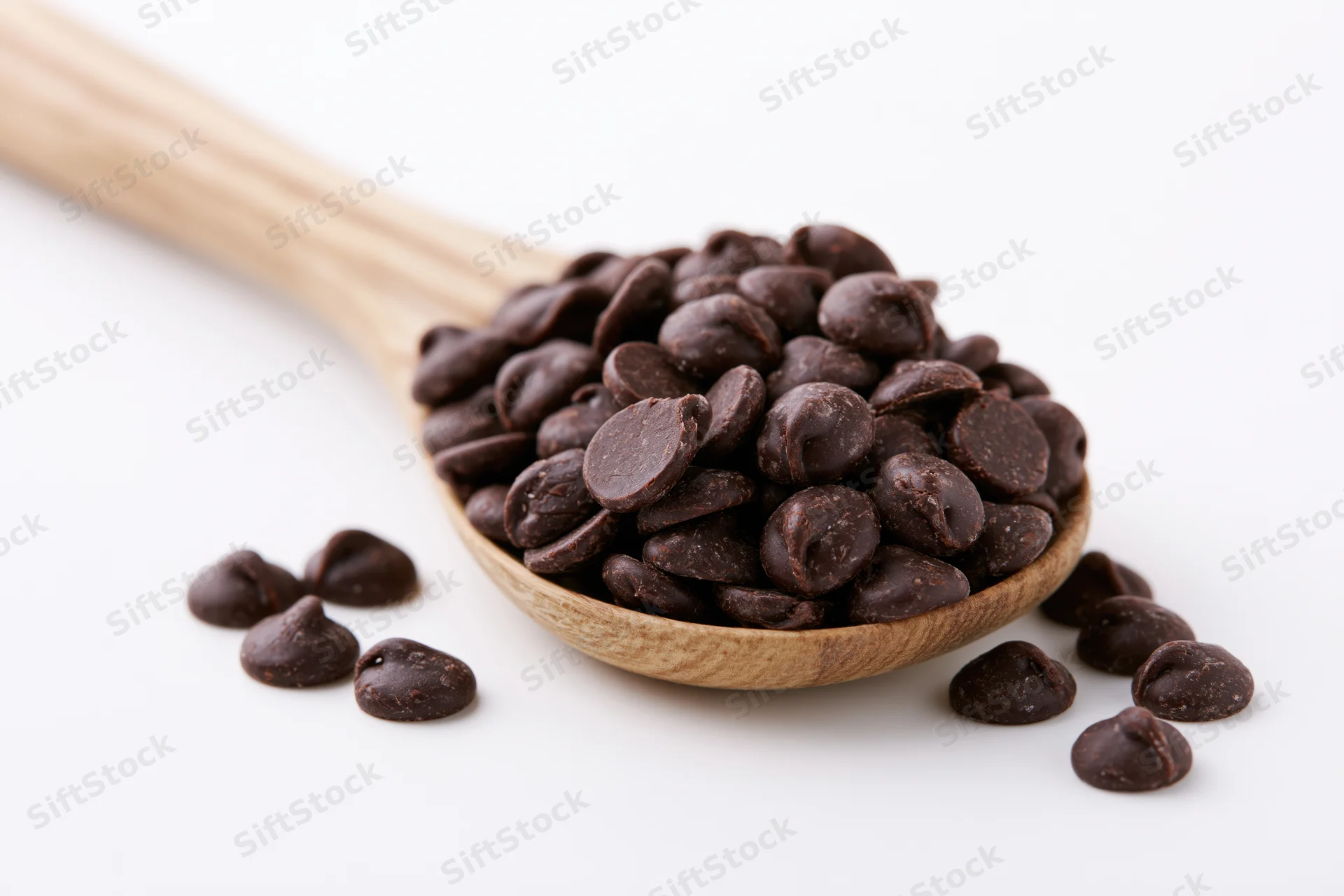 Dark chocolate chips piled in a wooden spoon on a white background