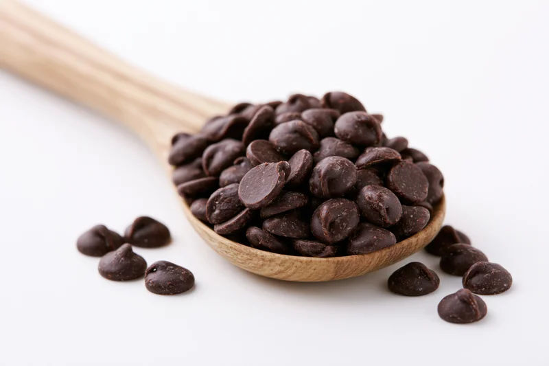 Dark chocolate chips piled in a wooden spoon on a white background