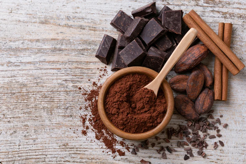 Dark chocolate chunks and cocoa powder in a wooden bowl with spoon on rustic wood surface