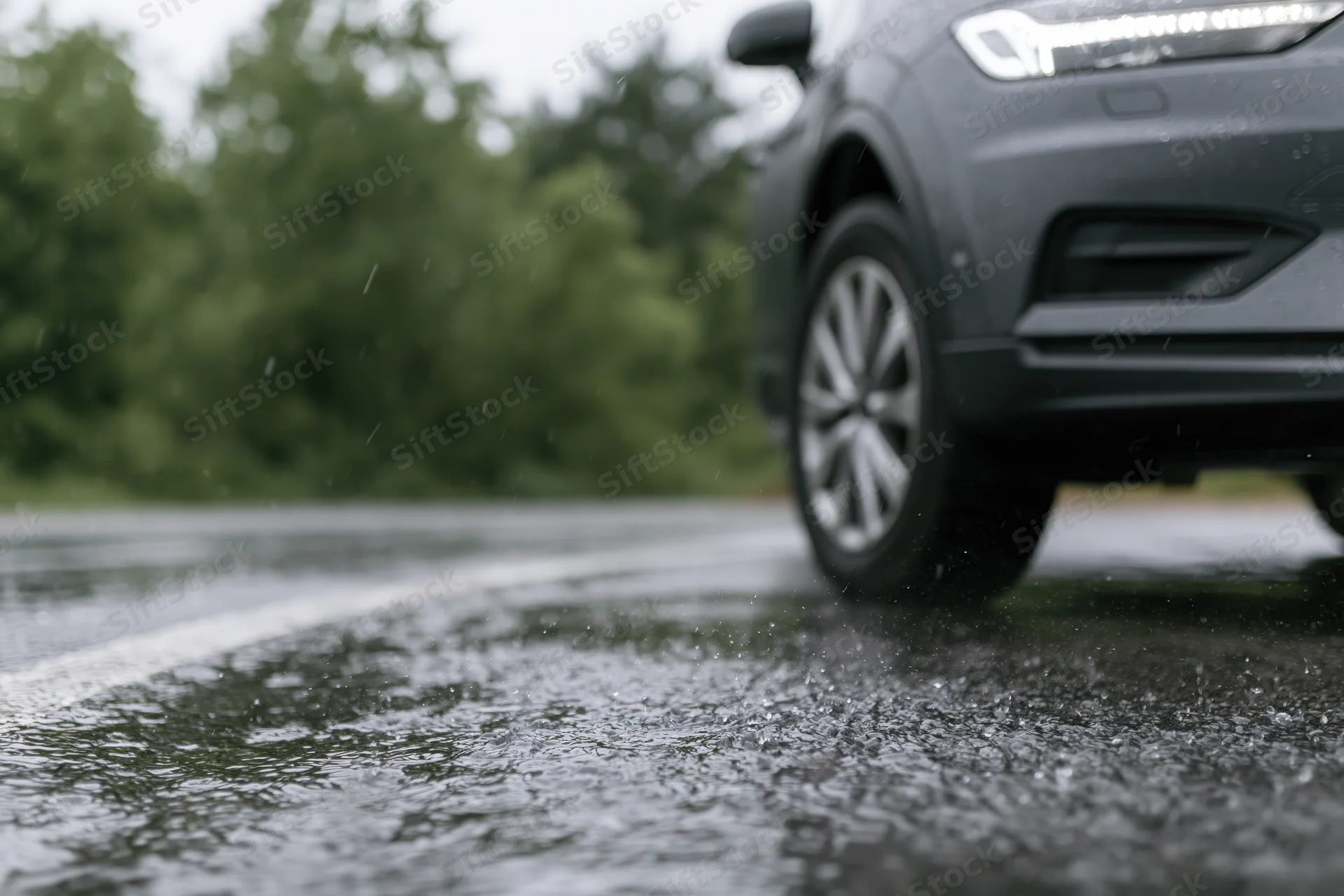 Dark grey suv parked on wet asphalt during heavy rain with water spraying from tire