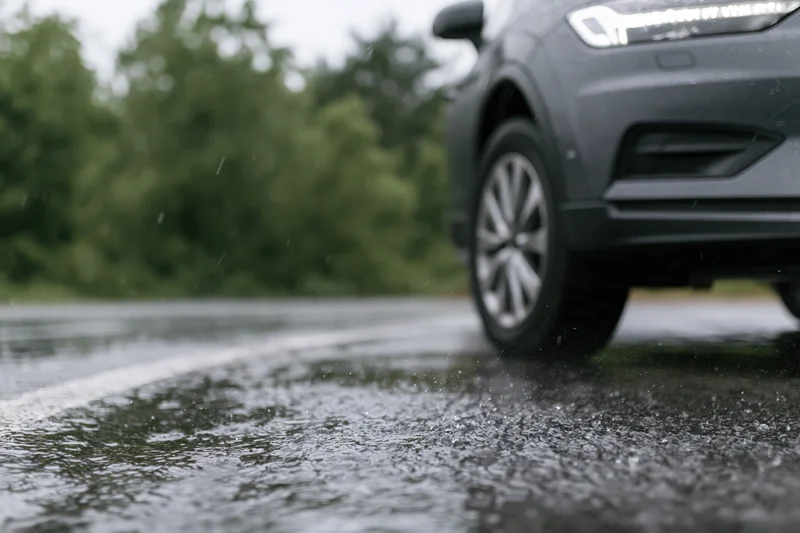 Dark grey suv parked on wet asphalt during heavy rain with water spraying from tire