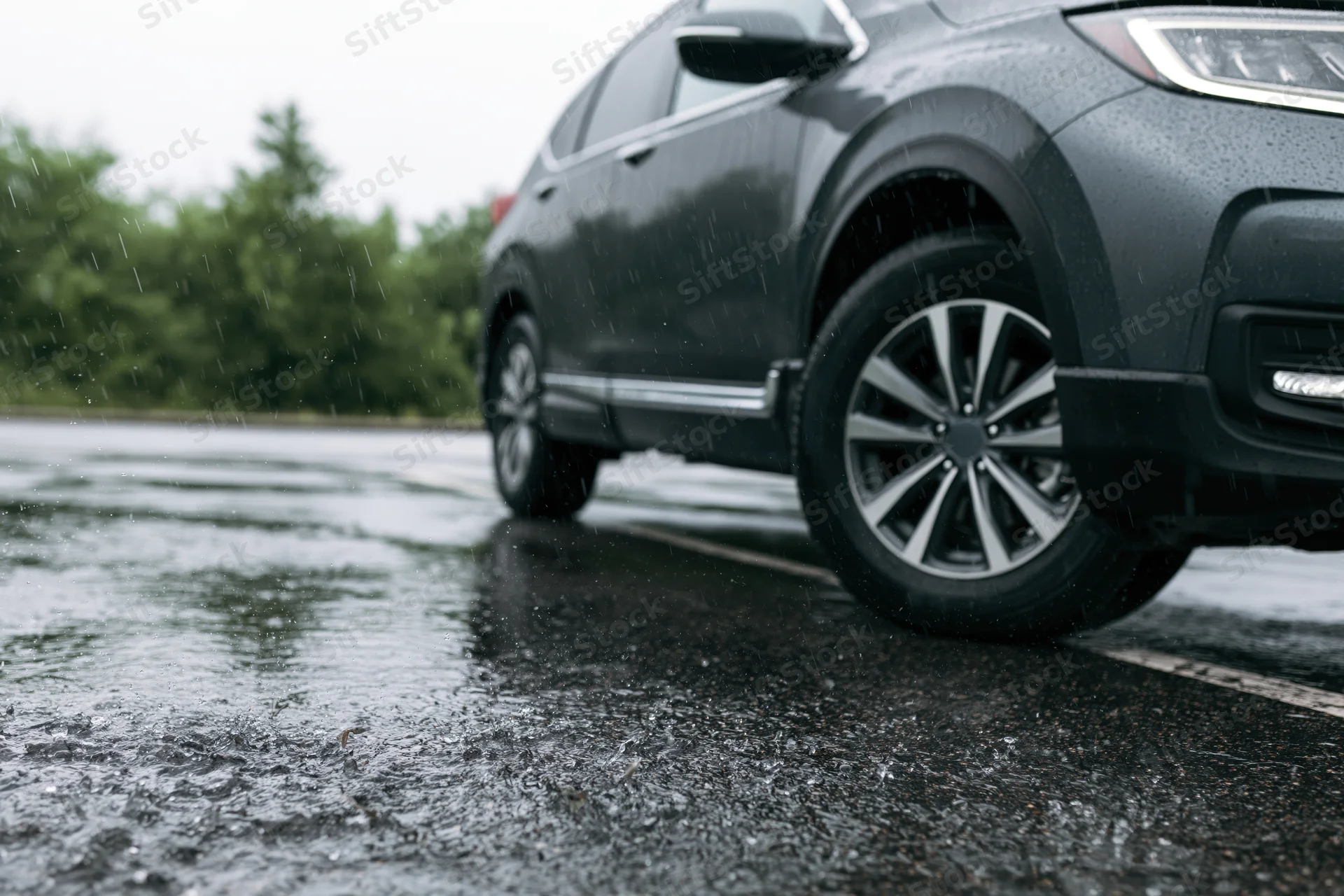 Dark grey suv parked on wet asphalt during heavy rain, low angle view of front wheel and tire