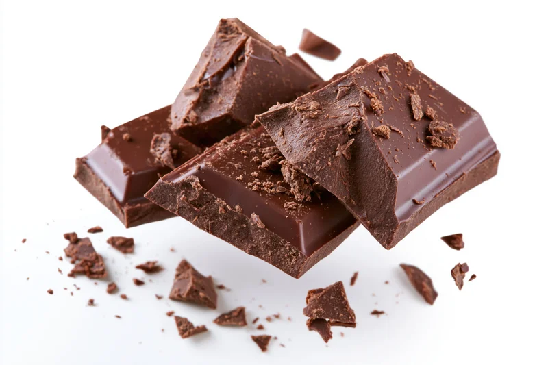 Broken dark milk chocolate chunks scattered on white background