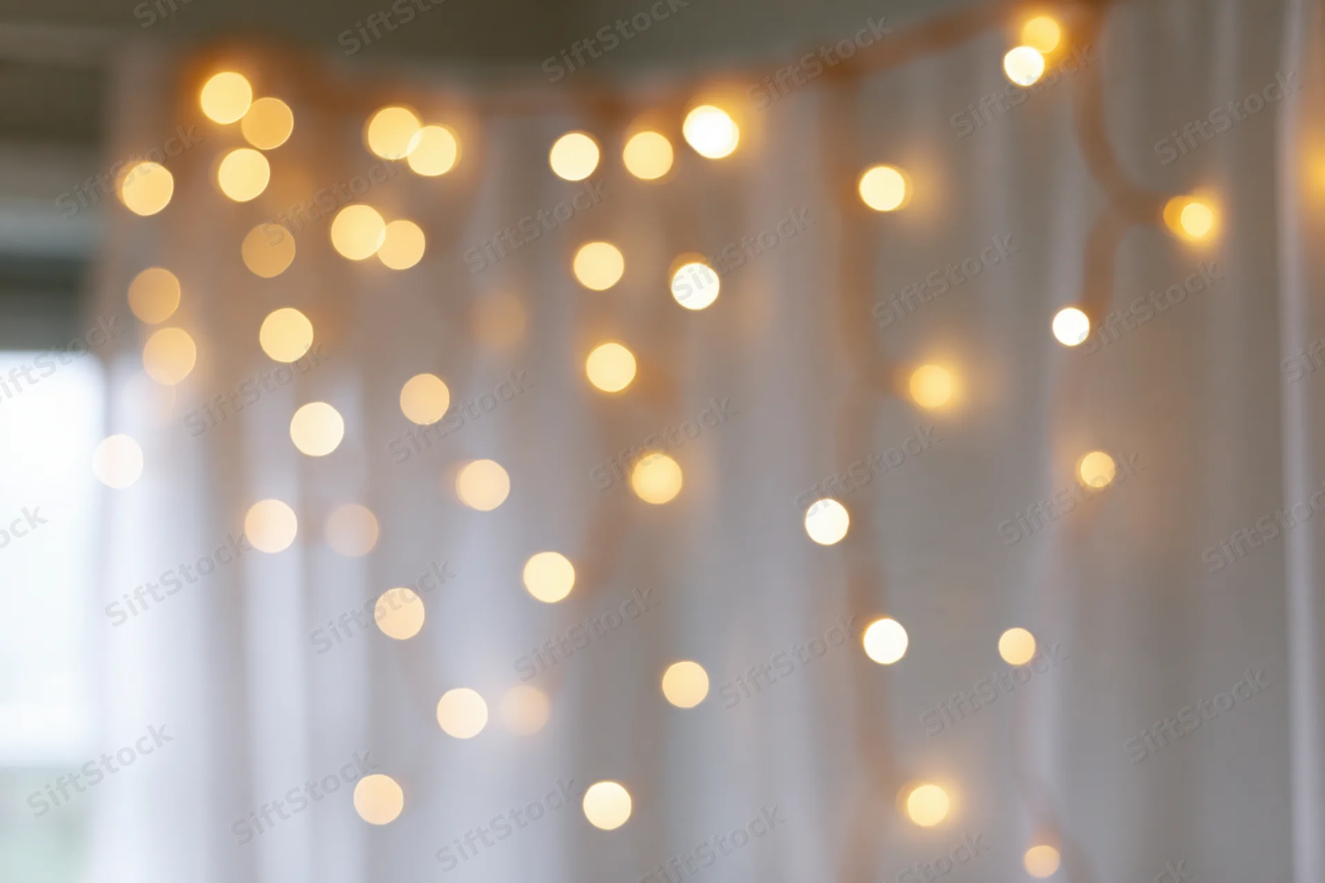 Defocused string lights glowing against a sheer white curtain indoors