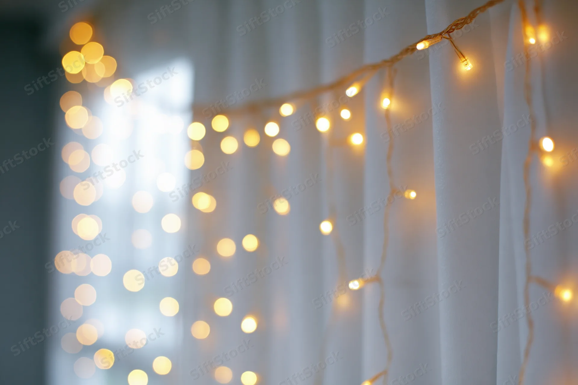String lights draped over a white curtain creating a soft glowing ambiance indoors