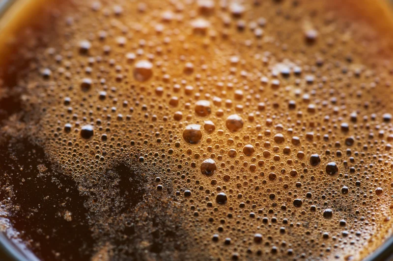Close-up of coffee crema with fine bubbles on the surface of a dark beverage in a cup