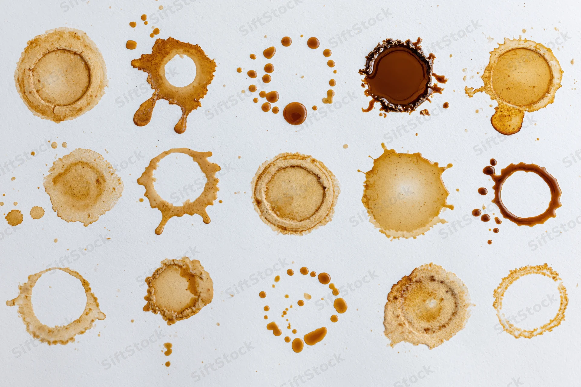 Fifteen coffee stains and splatter marks arranged in three rows on white paper