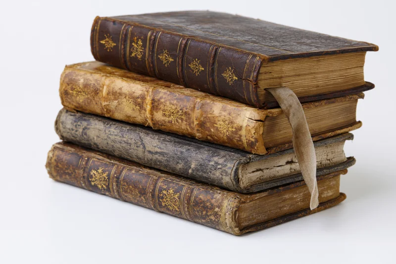Four antique leather-bound books stacked horizontally with spines visible on white background