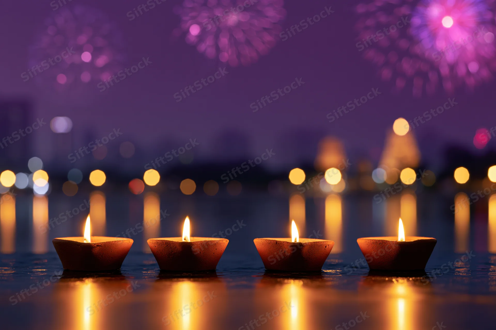 Four clay diya lamps floating on water with fireworks in the night sky during diwali celebration