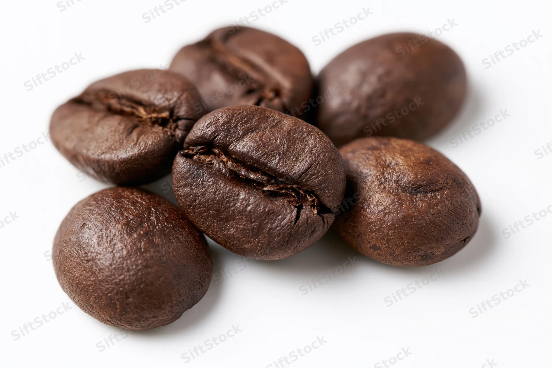 Dark roasted coffee beans arranged loosely on a white surface