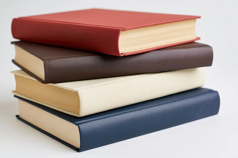 Four hardcover books stacked unevenly on a white surface