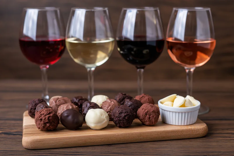 Four wine glasses with red white dark red and rosé wine arranged behind chocolate truffles on a wooden board
