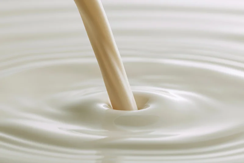 Milk pouring in a smooth stream onto a pooling surface creating ripples