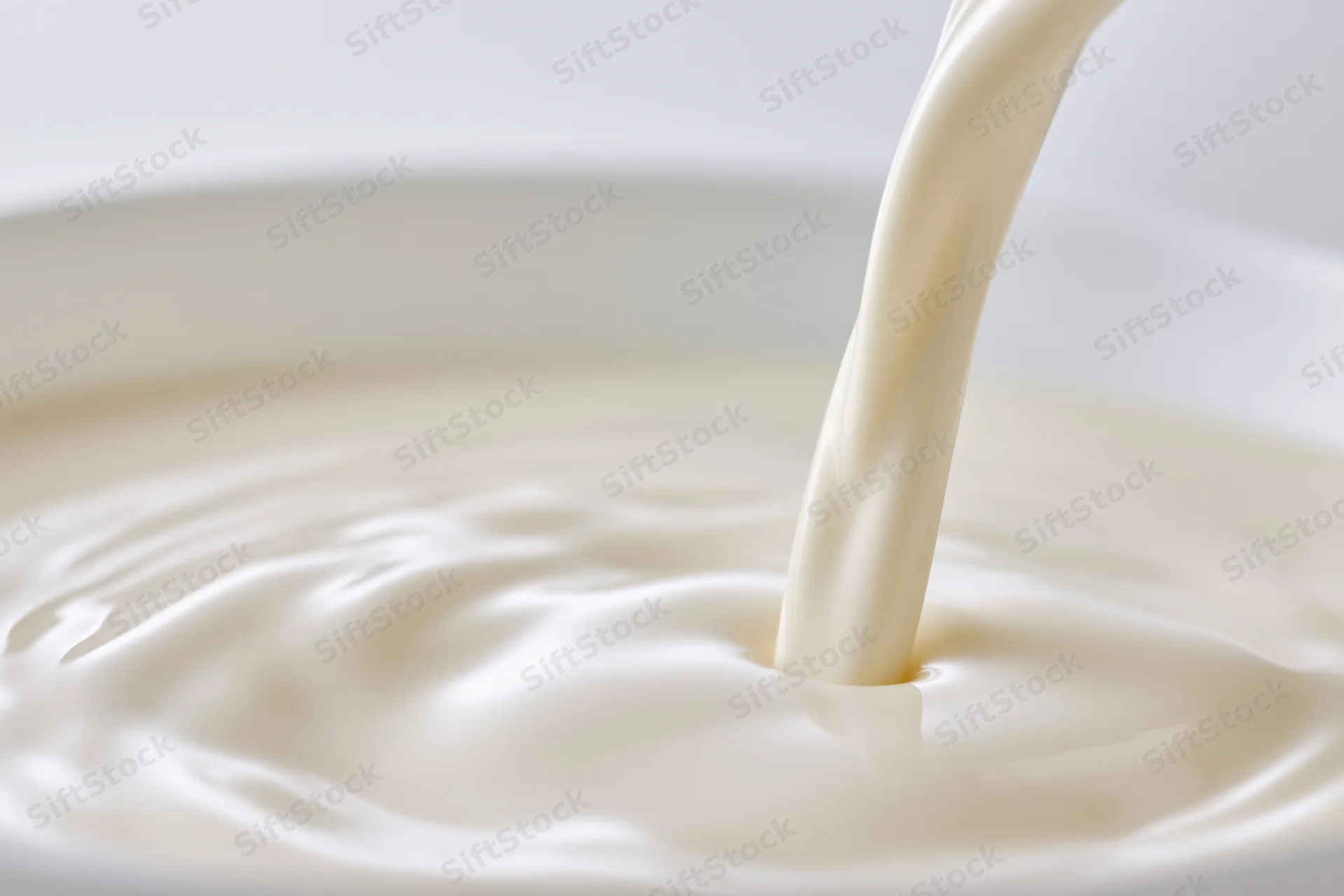 Milk pouring in a smooth stream into a white bowl, creating ripples on the surface
