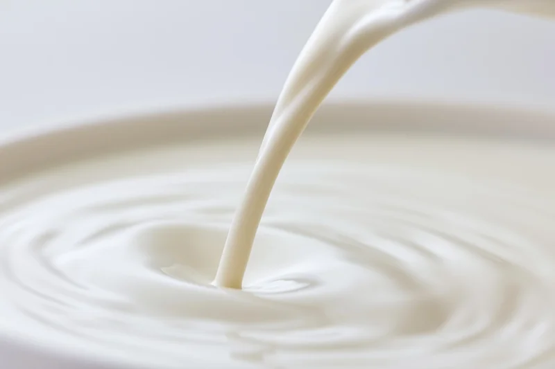 Milk pouring in a smooth stream into a bowl creating ripples on the surface