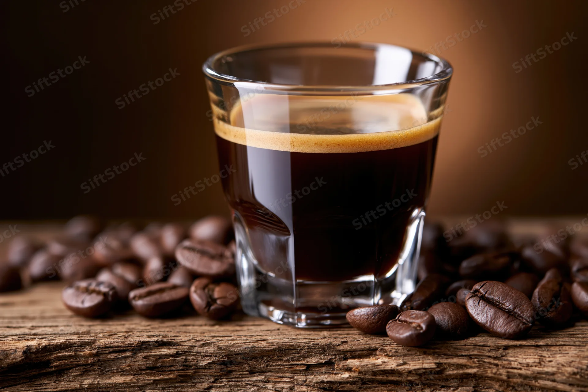 Espresso in a glass cup surrounded by coffee beans on a wooden surface