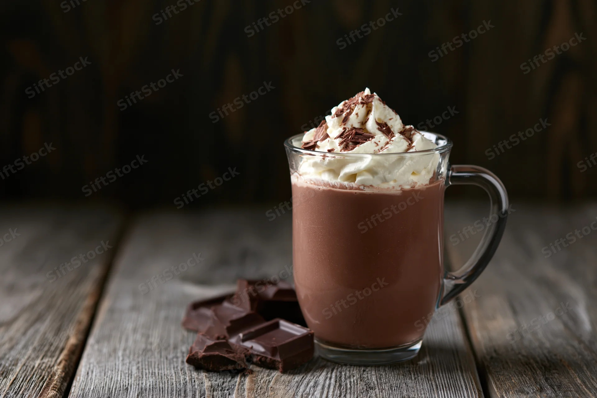 Glass mug of hot chocolate topped with whipped cream and chocolate pieces on a wooden table