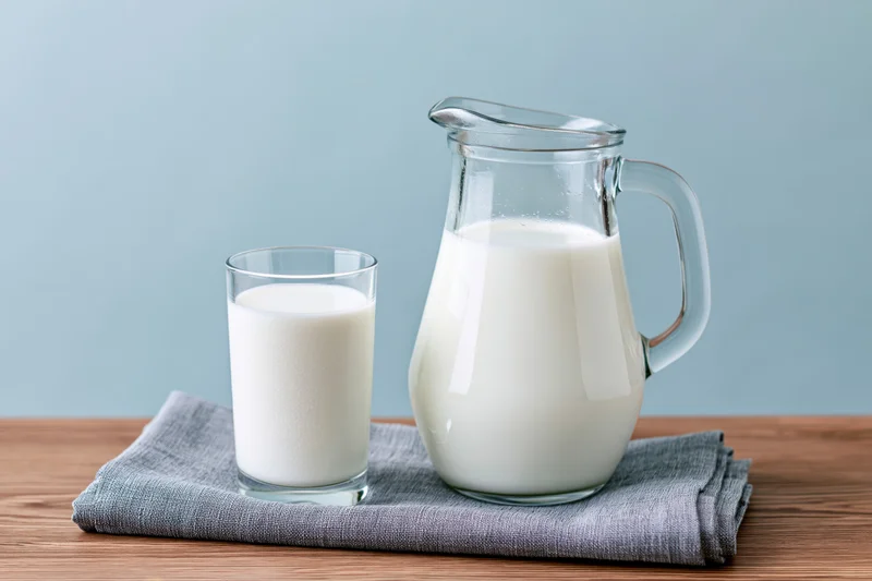 Glass pitcher and drinking glass filled with milk on a wooden table with a gray cloth