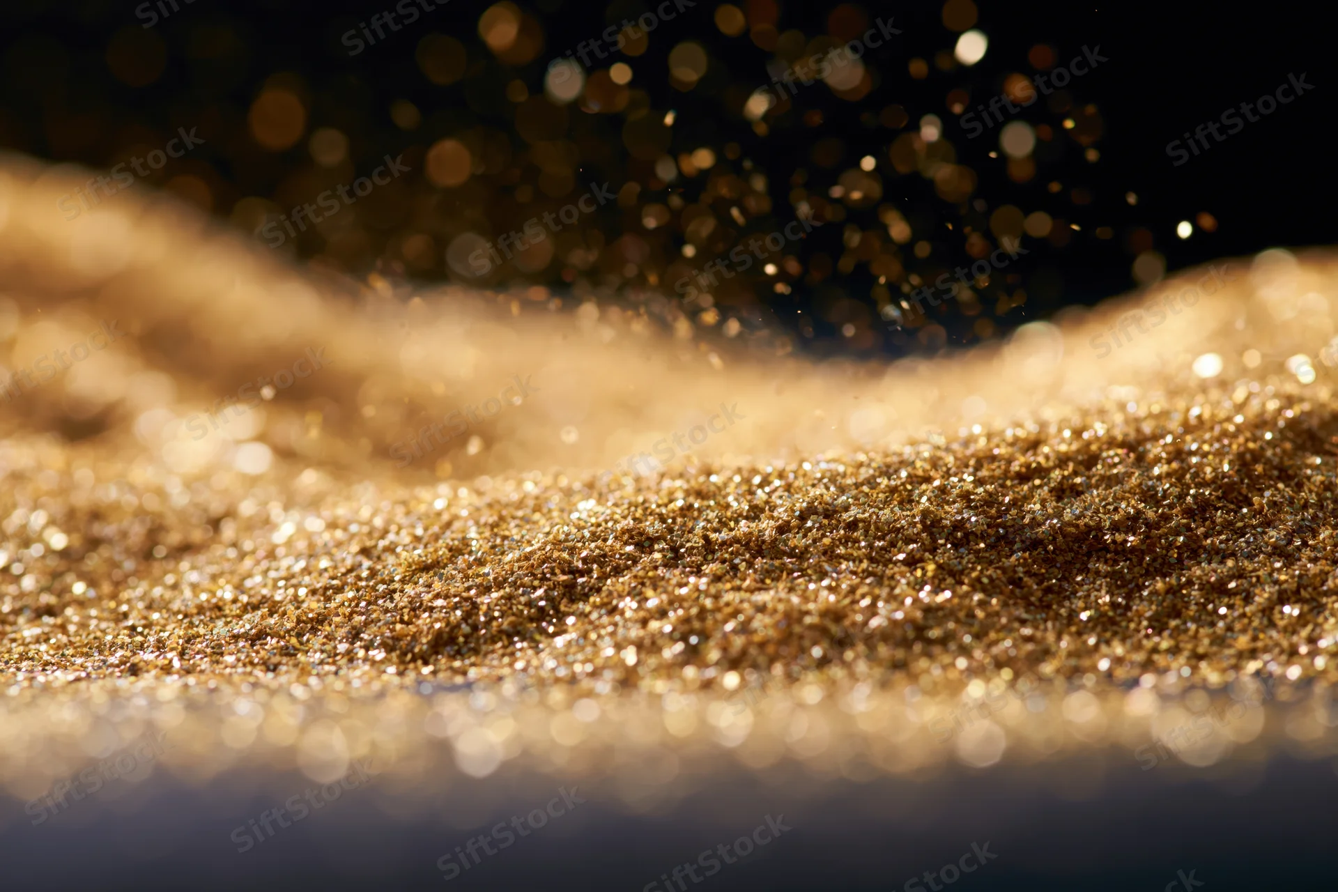 Gold glitter particles scattered across a flat surface with bokeh lights in the background