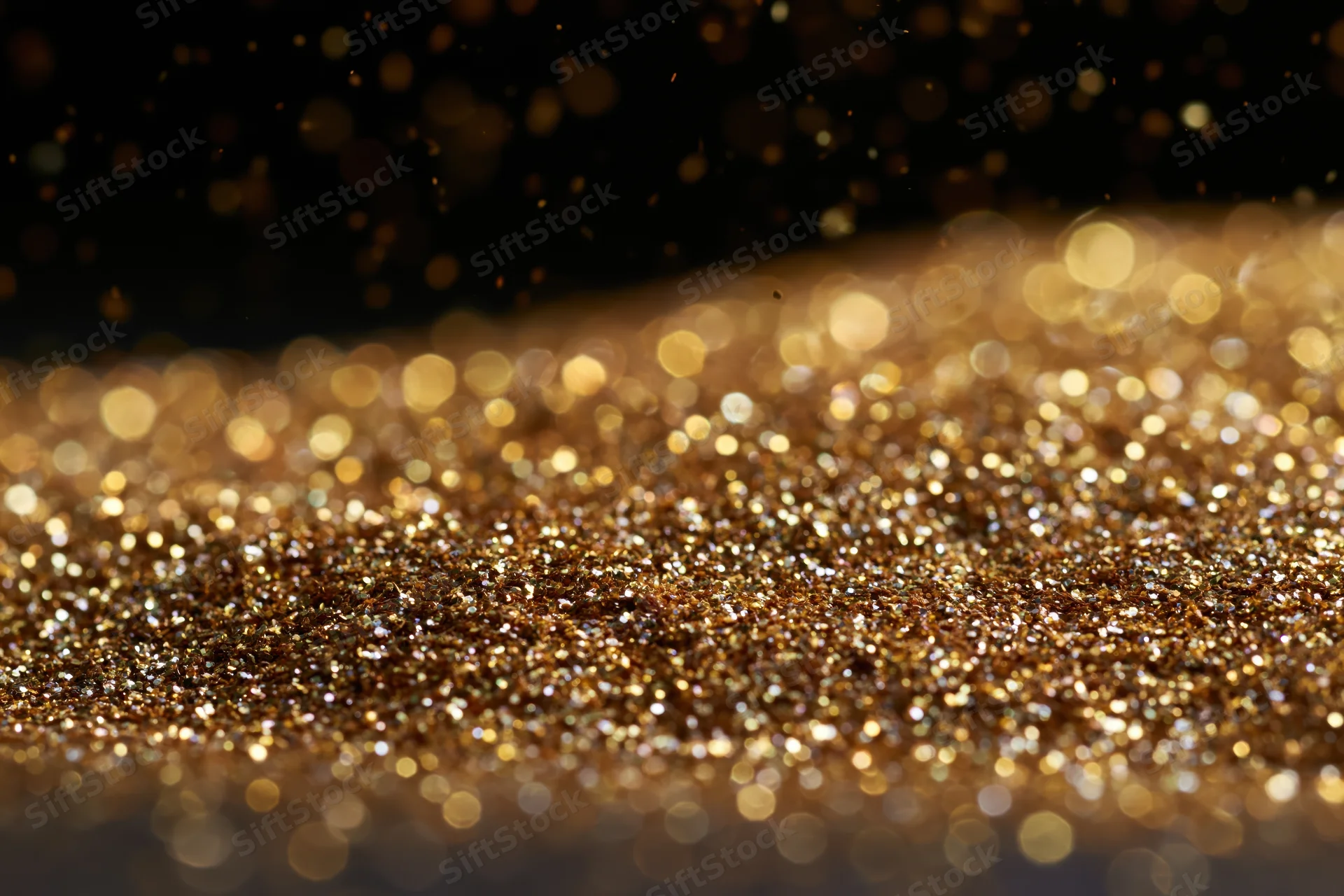Gold glitter particles scattered across a flat surface with bokeh effect in dark background