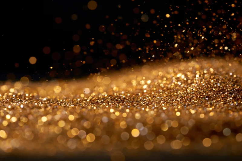 Gold glitter particles scattered across a flat surface with bokeh effect in dark background