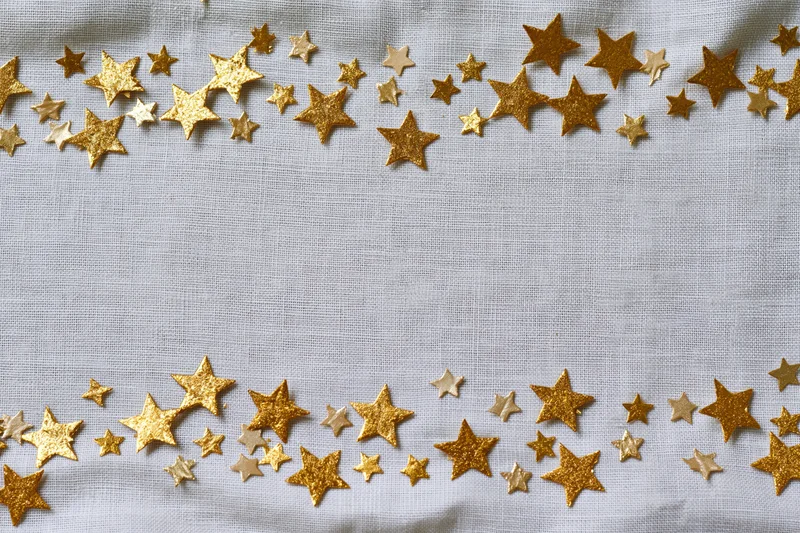 Gold metallic star confetti scattered along top and bottom edges of white fabric surface
