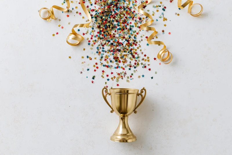 Golden trophy cup with colorful star confetti and gold ribbons on white surface