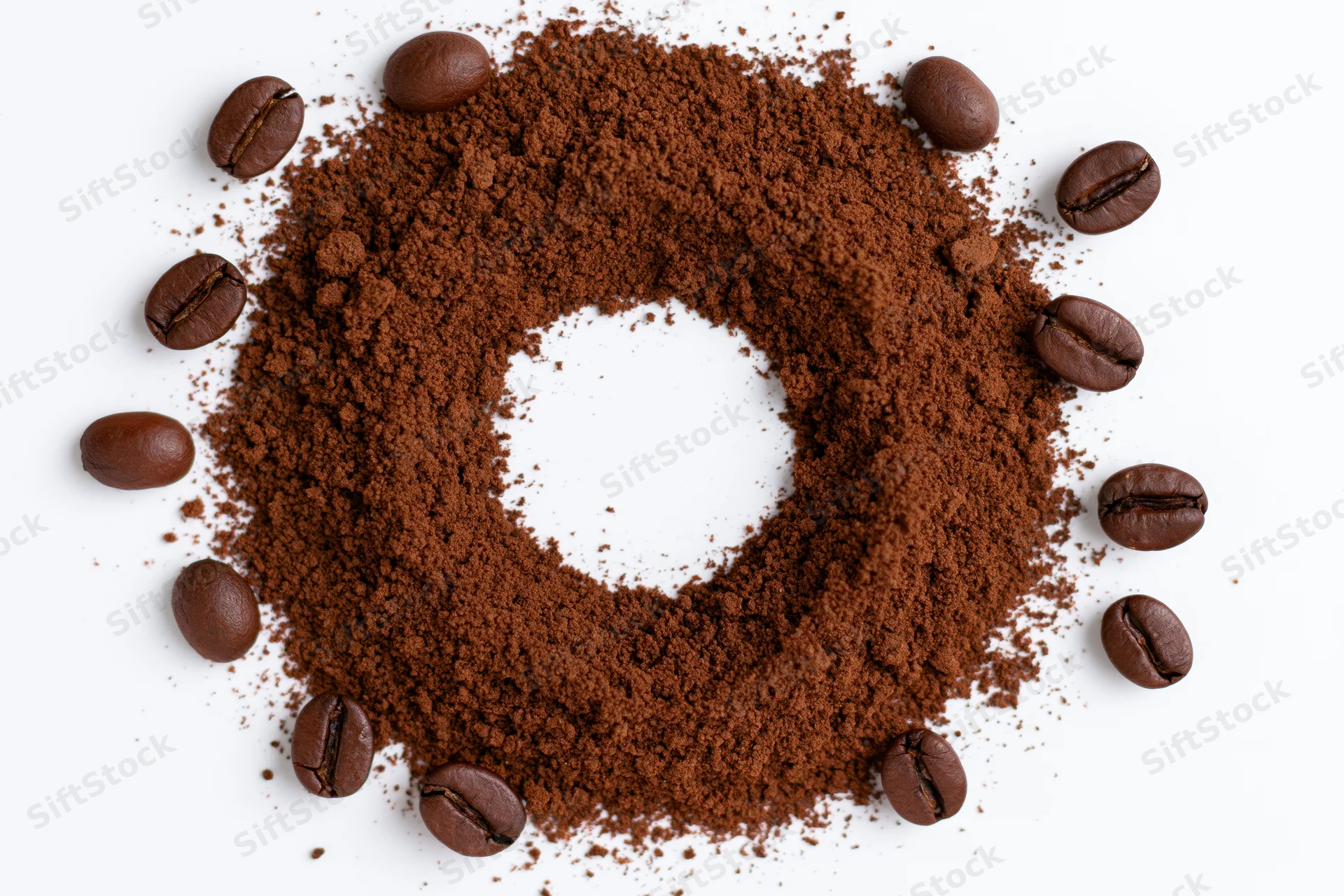 Ground coffee arranged in a circular ring with whole beans on white background