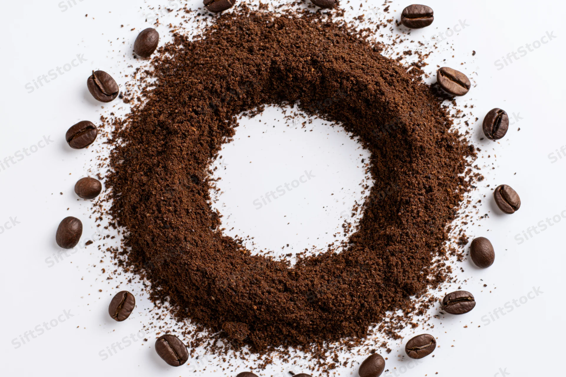 Ground coffee arranged in a circular ring with whole beans scattered around on white background