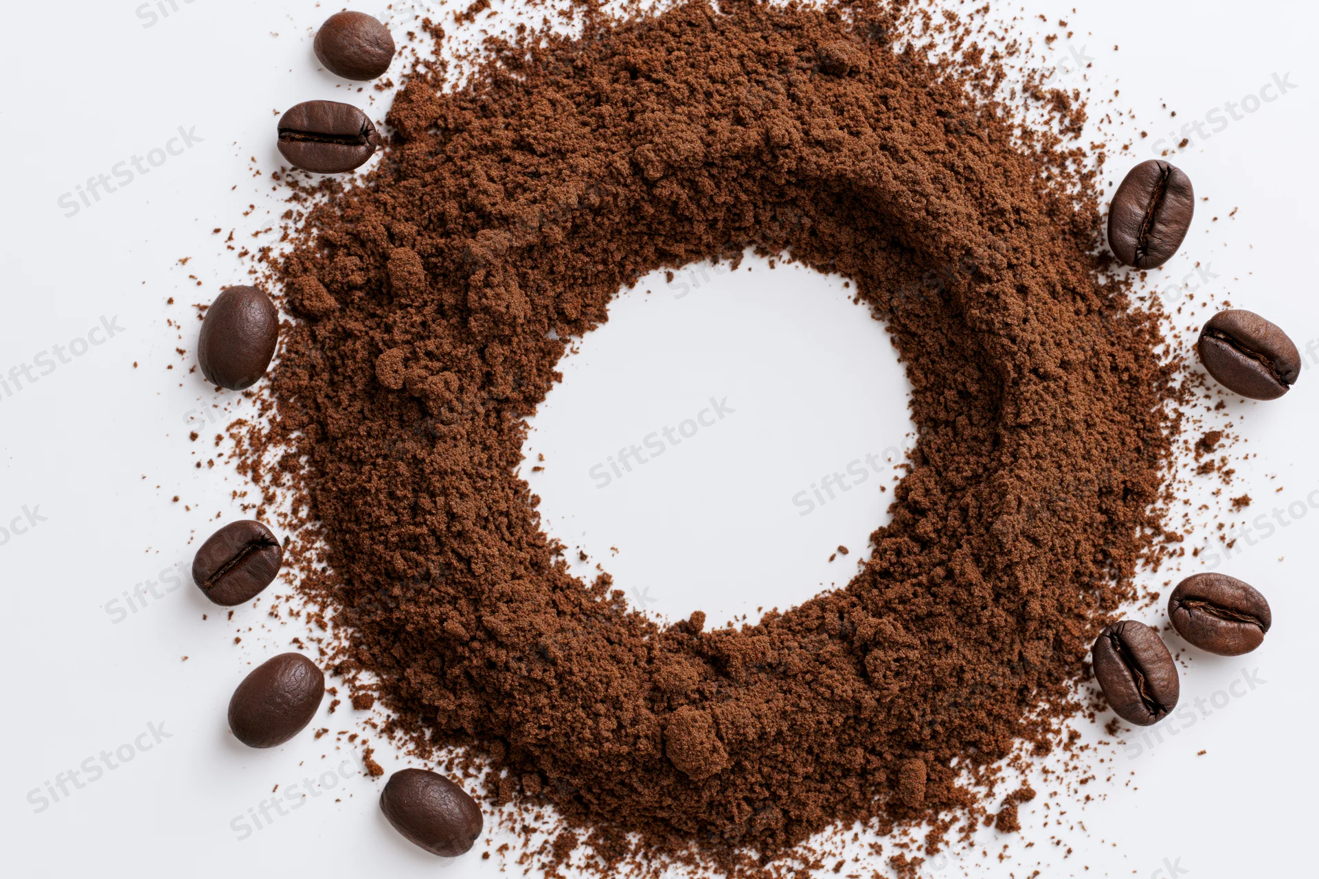 Ground coffee arranged in a circular ring with whole beans scattered around on white surface