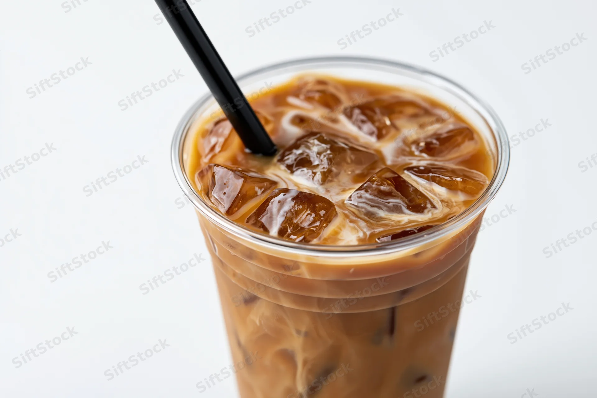 Iced coffee with cream swirling through ice cubes in a clear plastic cup with black straw on white background