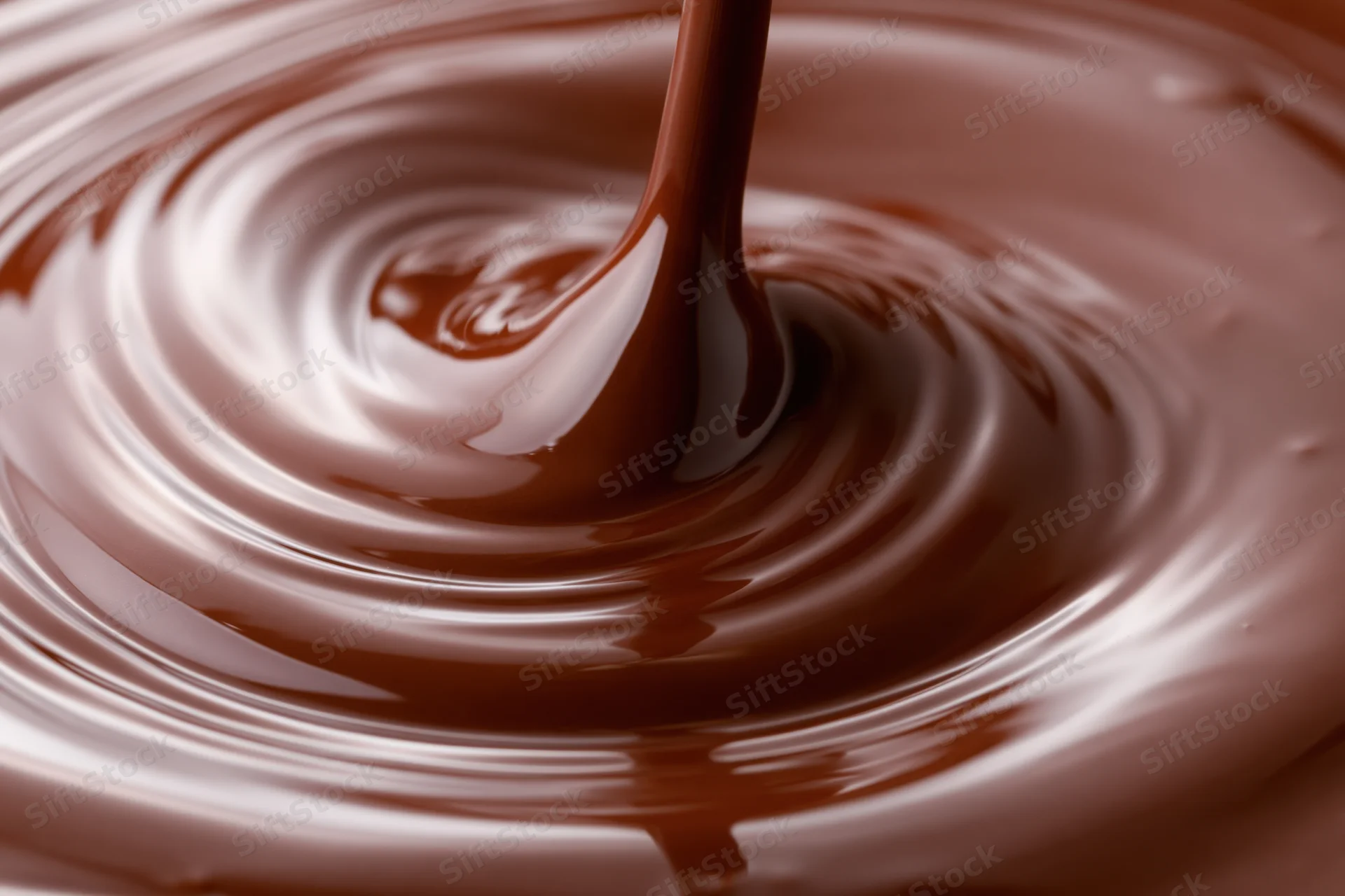 Liquid chocolate pouring in a slow stream creating ripples on a smooth surface