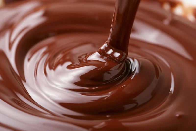 Liquid dark chocolate pouring in a slow stream creating swirling ripples on a glossy surface
