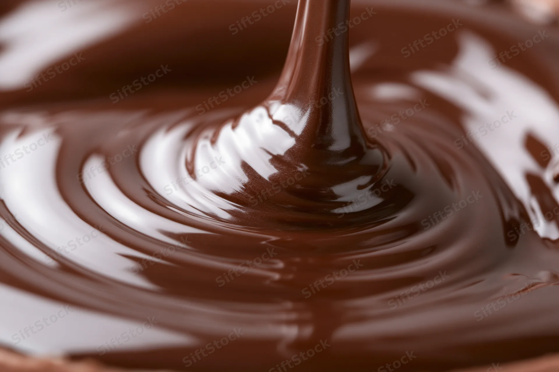 Dark chocolate pouring in a slow stream creating ripples on a glossy surface
