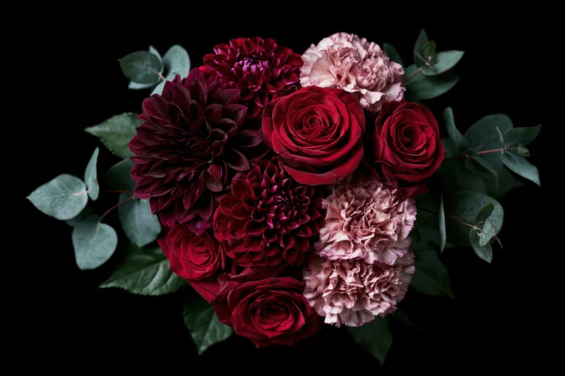 Lush bouquet of deep red roses, burgundy dahlias, and dusty pink peonies with eucalyptus leaves on black background