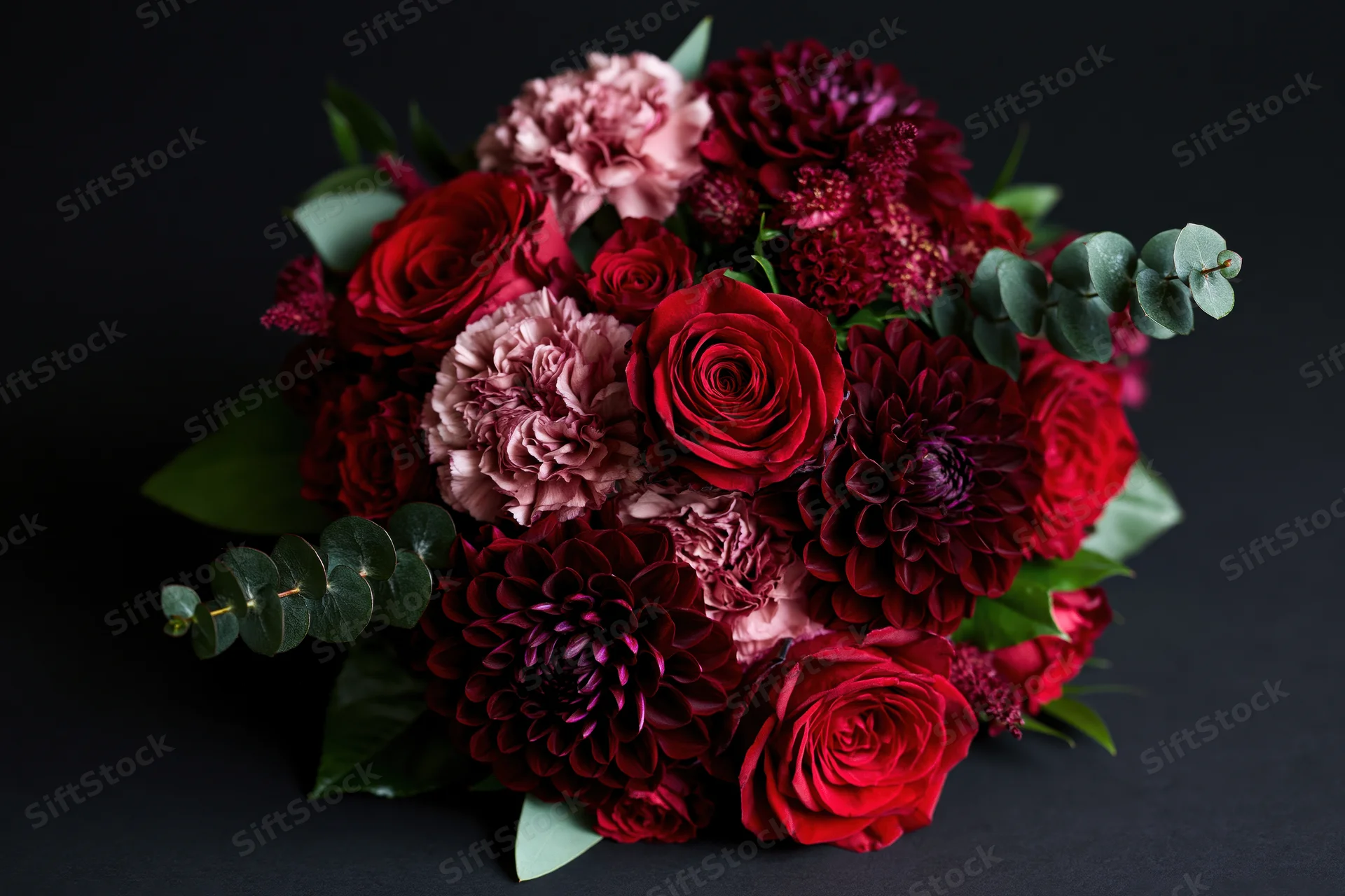 Lush bouquet of deep red roses and burgundy dahlias with eucalyptus leaves on dark surface