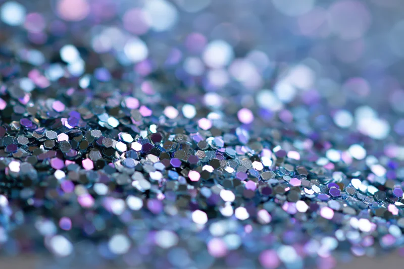Macro closeup of dense holographic glitter scattered across a surface with bokeh background