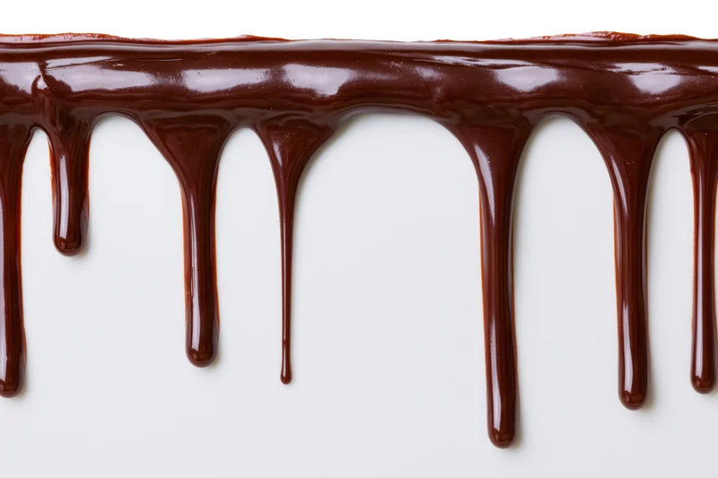 Melted dark chocolate dripping in glossy streams against a white background