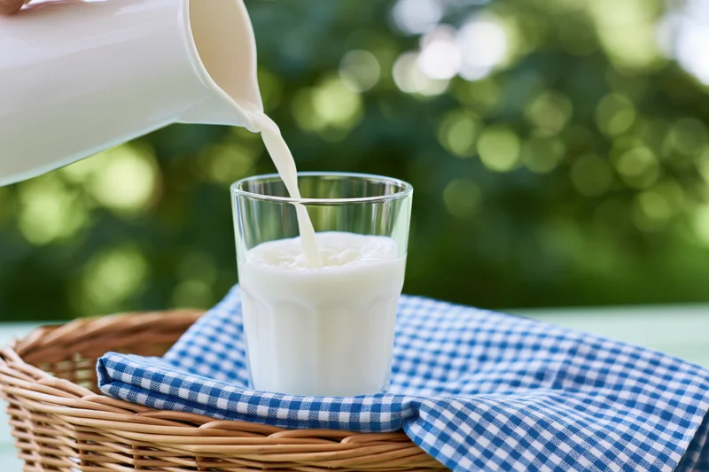 Milk being poured from a white jug into a clear glass mid-pour