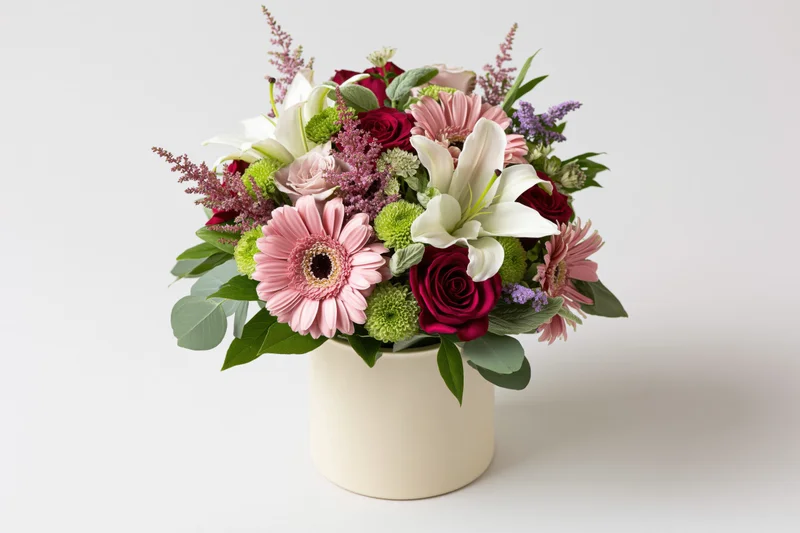 Mixed flower bouquet in a cream cylindrical vase centered on white background