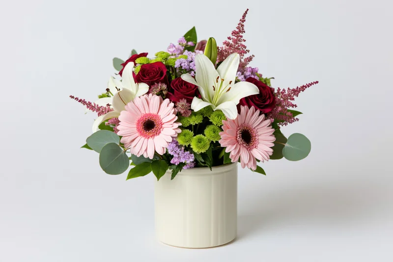 Mixed flower bouquet in a cream cylindrical vase centered on white background
