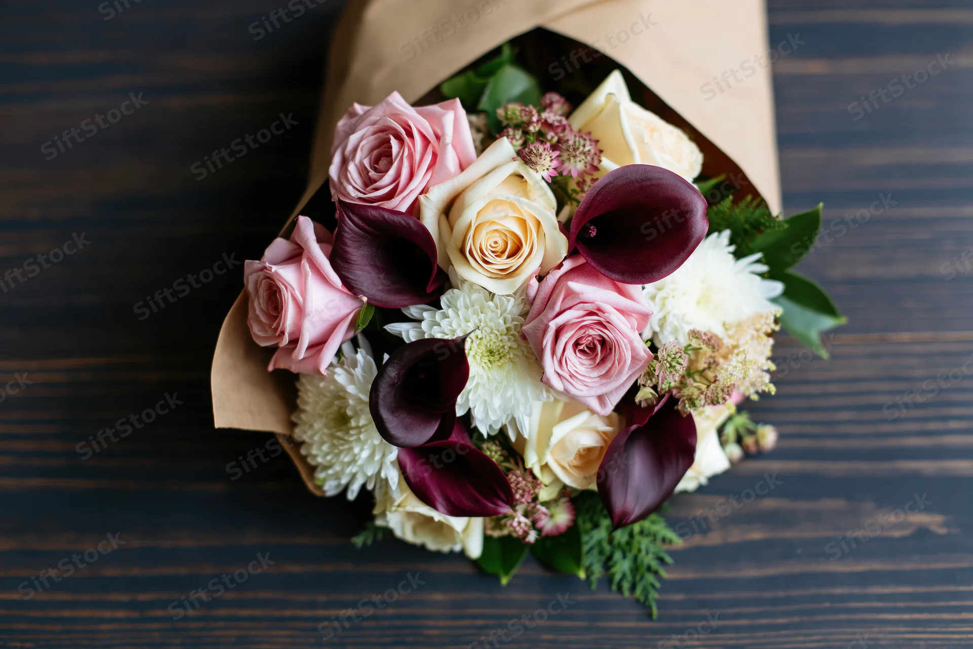 Mixed flower bouquet wrapped in kraft paper on dark wooden table