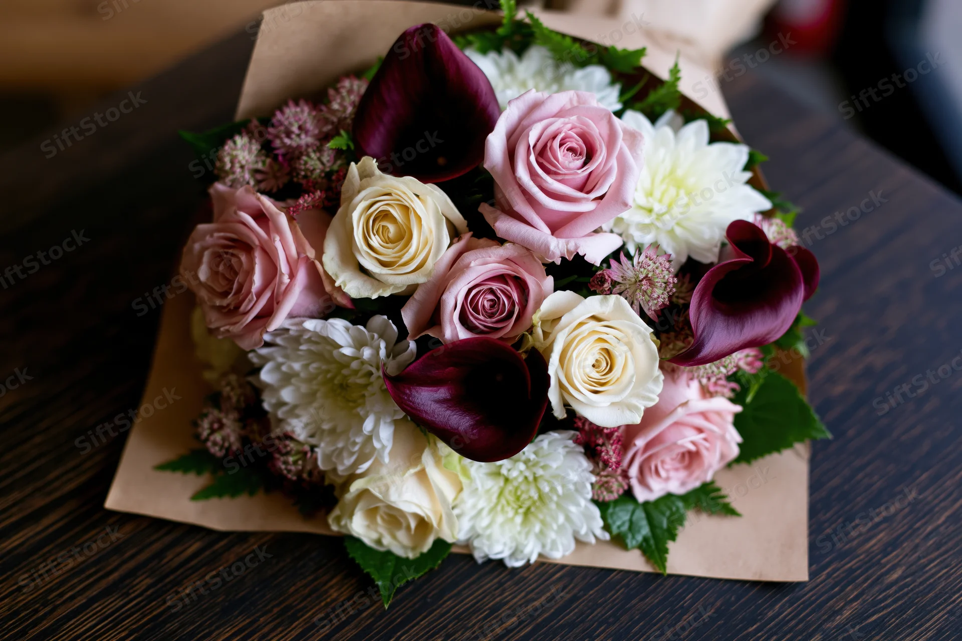 Mixed flower bouquet wrapped in kraft paper resting on dark wooden table