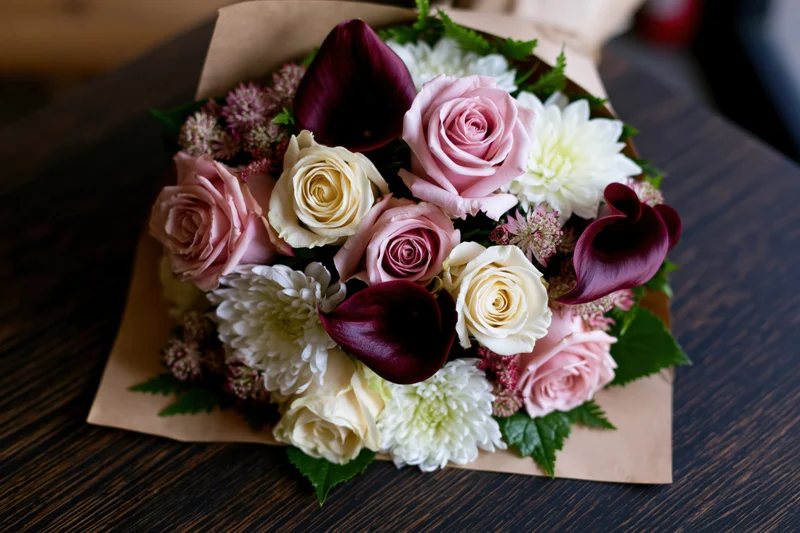Mixed flower bouquet wrapped in kraft paper resting on dark wooden table