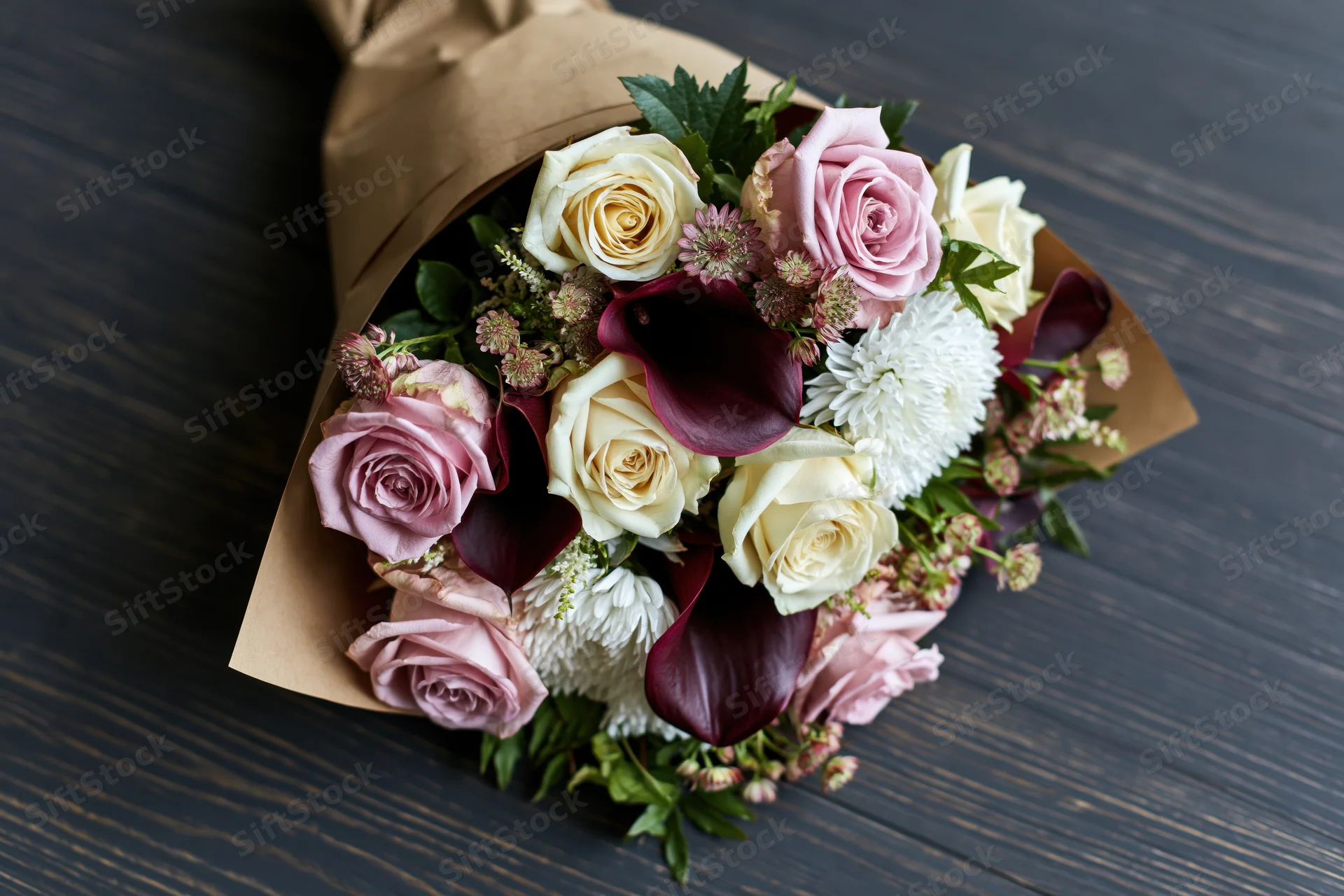 Mixed flower bouquet wrapped in kraft paper resting on dark wooden surface