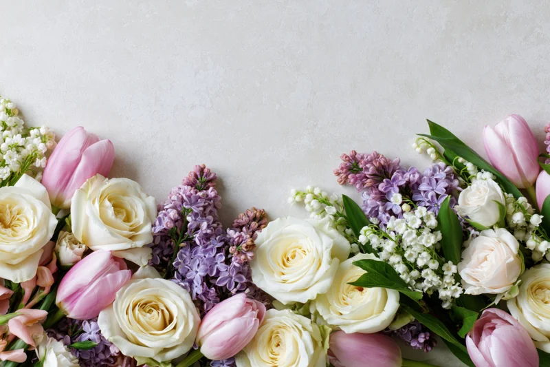 Spring bouquet of roses, tulips, lilacs and lily of the valley arranged along bottom edge on light surface