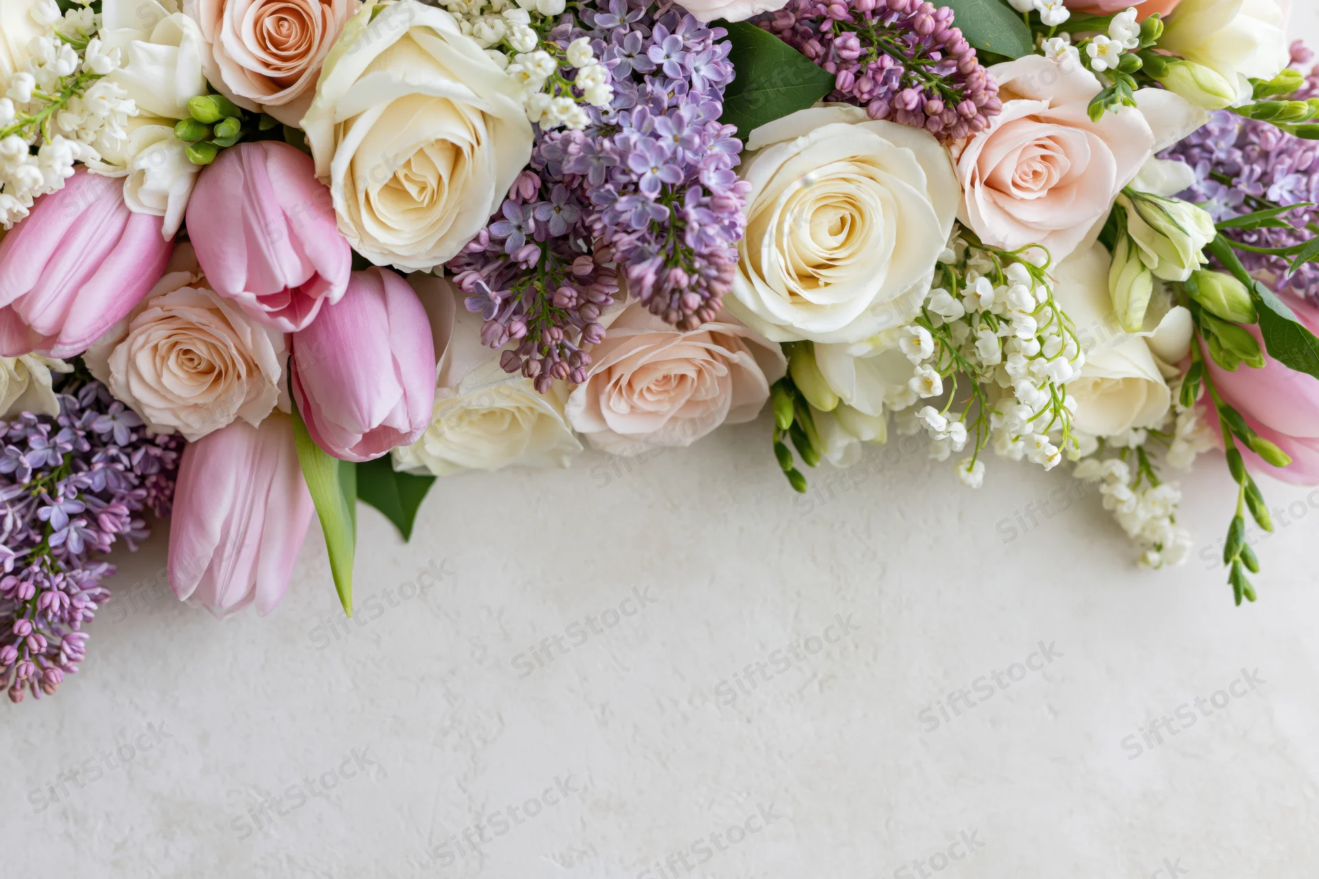 Spring bouquet of roses, tulips and lilac arranged along bottom edge of white surface with copyspace